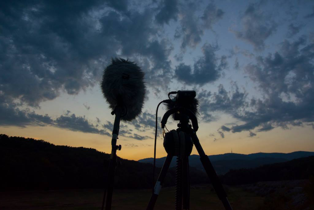 A boom microphone and the zoom recorder with a cloudy sky in he background.